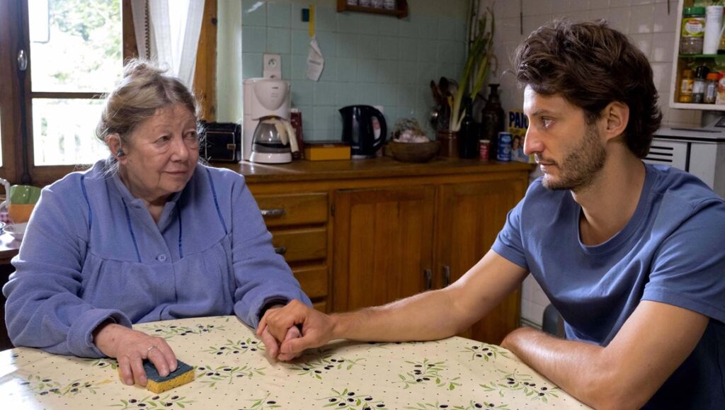 The Book of Solutions film still: An older woman and a younger man hold hands at a kitchen table. French Cinema 2024.