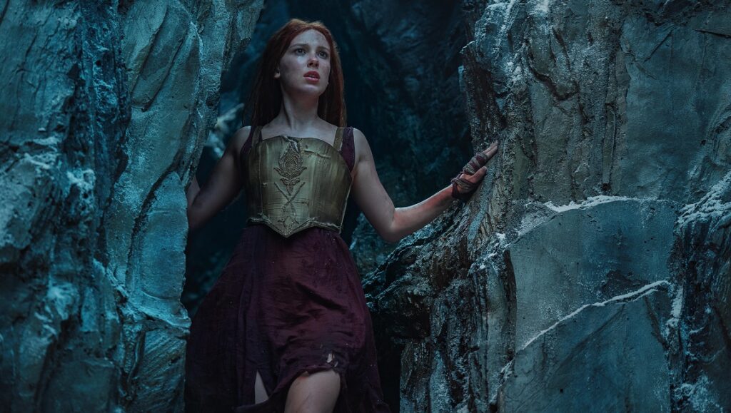 Millie Bobby Brown in Damsel. Woman in armor emerges from a cave.