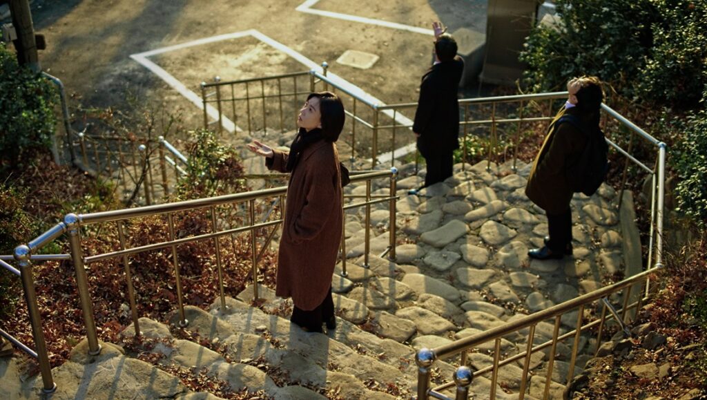 Gasoline Rainbow film review: Three people look up on stone steps with metal railings.