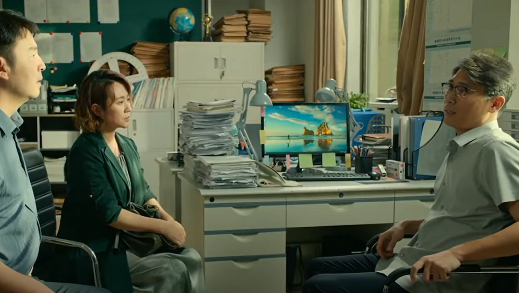 Scene from Article 20 by Zhang Yimou: Three people in an office setting, desk with piles of papers.