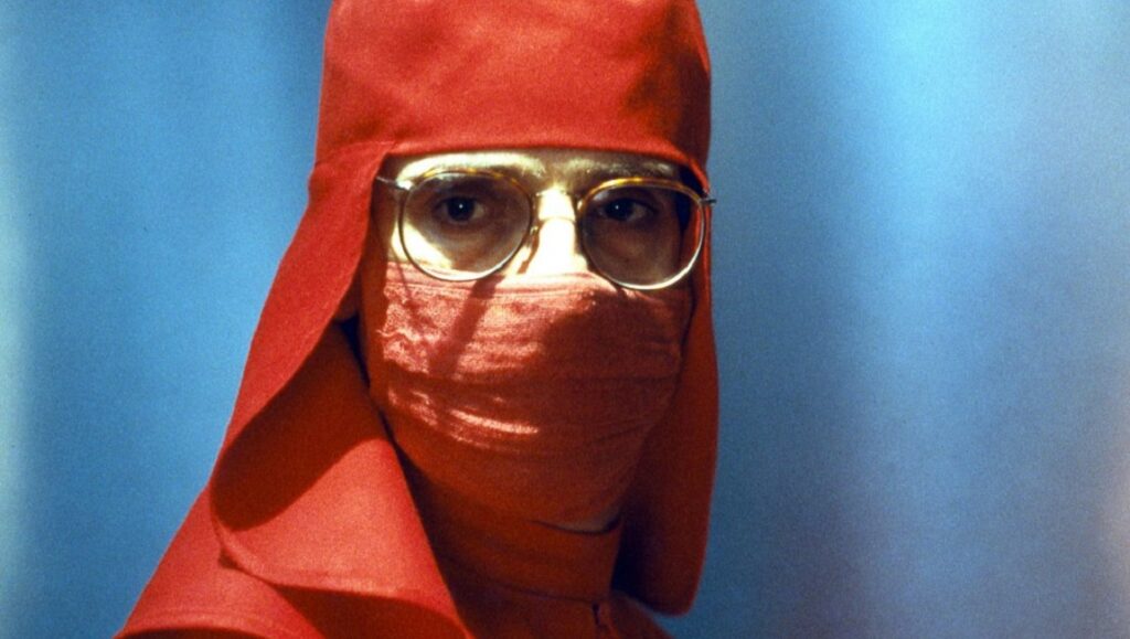 Jeremy Irons in Dead Ringers, a David Cronenberg film. Red surgical garb, glasses.