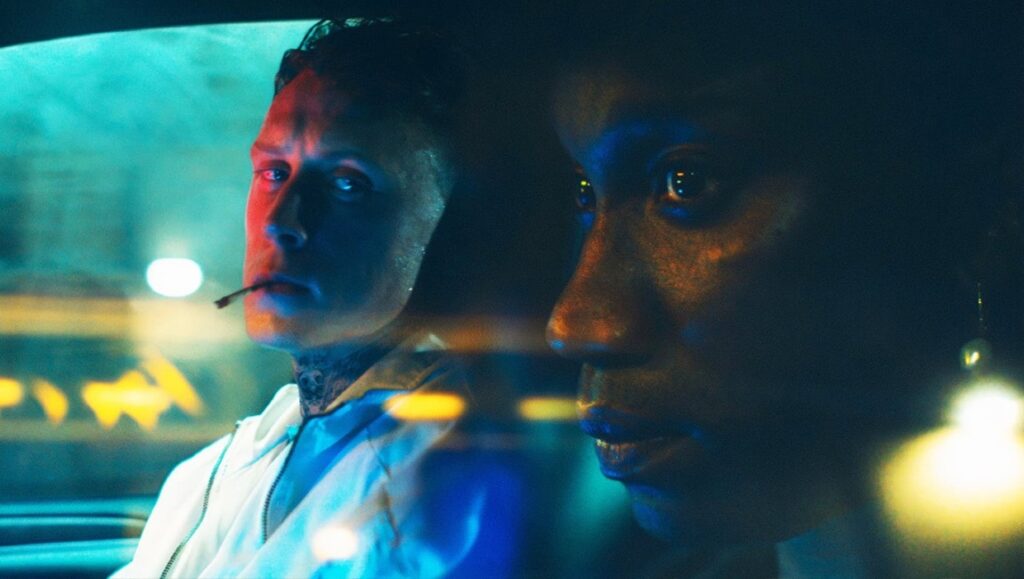 Film still from Femme featuring two actors in a car at night. One has a cigarette, the other gazes forward.