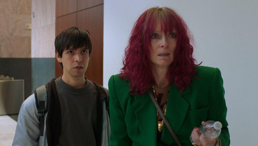 Still from Problemista film review: Julio Torres and Tilda Swinton. Swinton wears a green blazer and Torres a backpack.