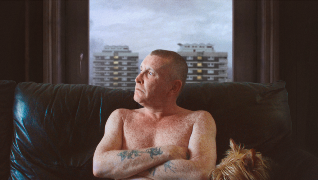The Flats CPH:DOX '24 review image. Man with tattoos, dog, and flats in the background. Alessandra Celesia film.