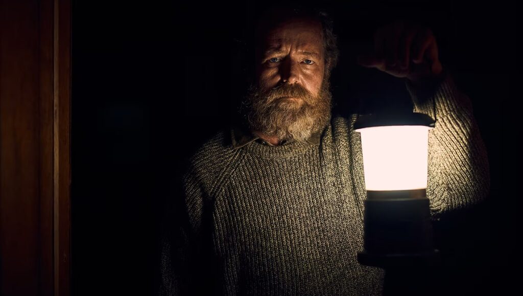 You'll Never Find Me movie review image: Man with beard holding lantern in the dark. Horror film.