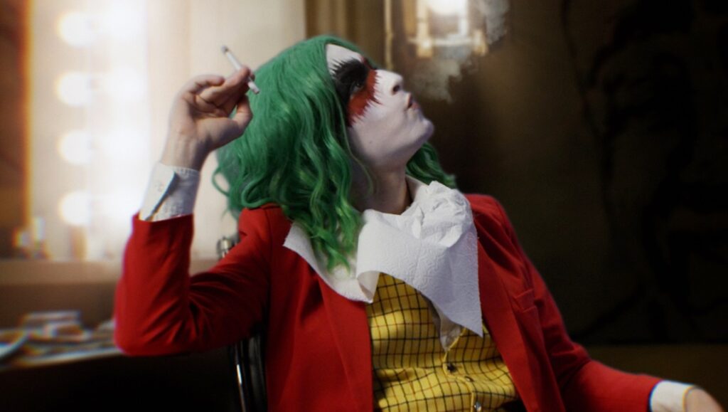 Vera Drew as Joker smoking. The People's Joker movie review. Green hair, red suit, white face paint.