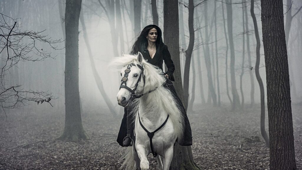 Eva Green as Milady in The Three Musketeers: Part II riding a white horse in a foggy forest.