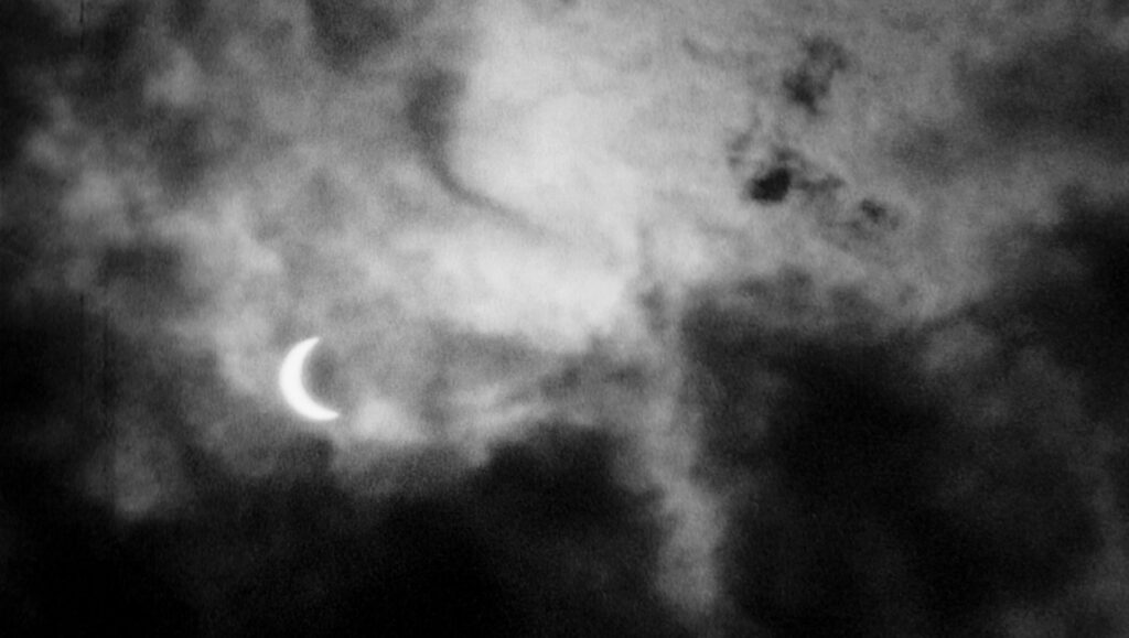 Black and white eclipse film still. Crescent moon peeks through dark clouds. Kevin Jerome Everson's Polly One.