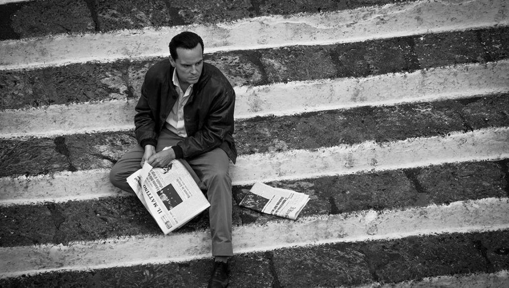 Black and white still from Ripley: Man sits on stairs holding Il Mattino newspaper.