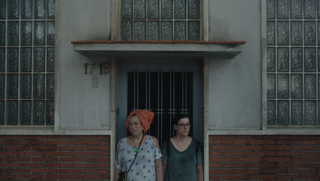 Of Living Without Illusion film still. Two women stand in front of a building with barred windows. New Directors/New Films 2024.