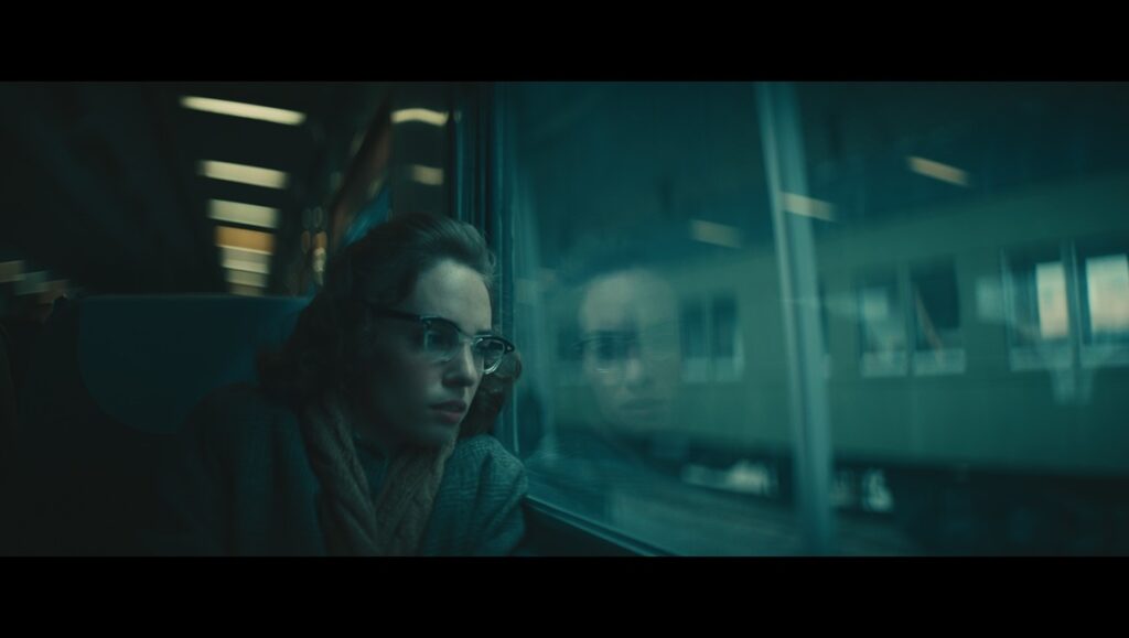 Still from Wildcat with a woman in glasses looking out a train window.