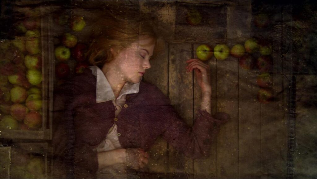 Dogville movie still. Nicole Kidman lies on wooden floor surrounded by apples.