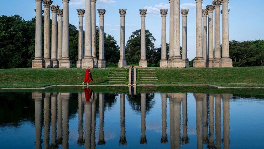Abiding Nowhere film still. Monk in red robe walks by reflecting pool near stone columns. Tsai Ming-liang Prismatic Ground '24 review.