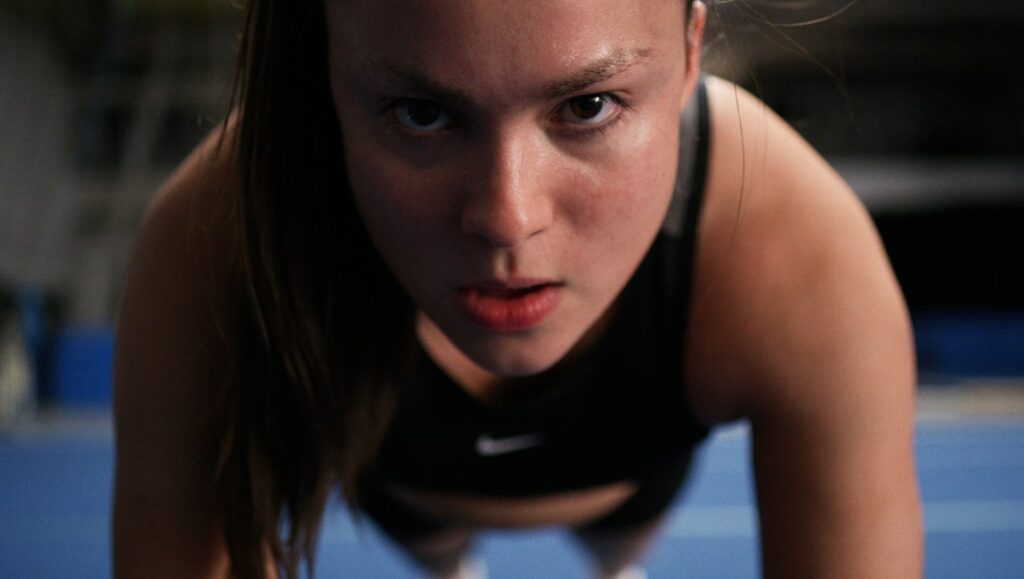 Backspot movie still. Intense female athlete in push-up position. Focus on determination.