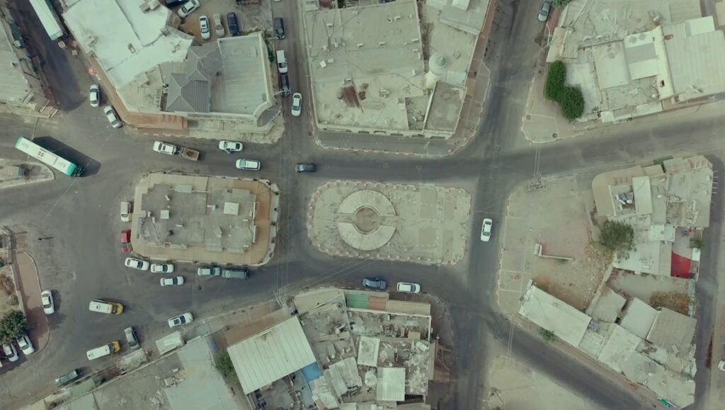 Aerial shot of Lyd, Israel, featured in the film by Sarah Ema Friedland & Rami Younis. Cars, buildings, and a roundabout.
