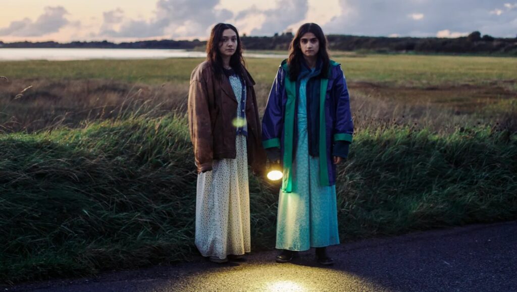 Two women stand with a lantern in September Says movie scene. Atmospheric, moody lighting, rural landscape.