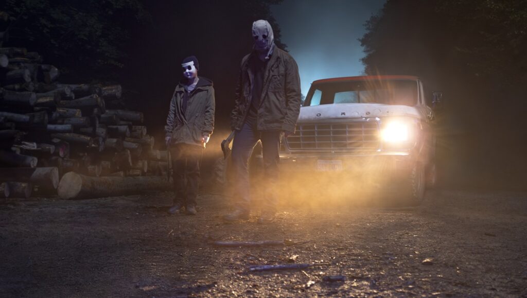The Strangers: Chapter 1 movie scene. Masked figures stand near a truck in the dark. Horror film.