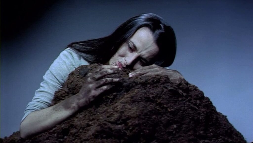 Antoinetta Angelidi's Thief of Reality film still. Woman embraces earth, face pressed against soil. Dark, surreal, emotional.
