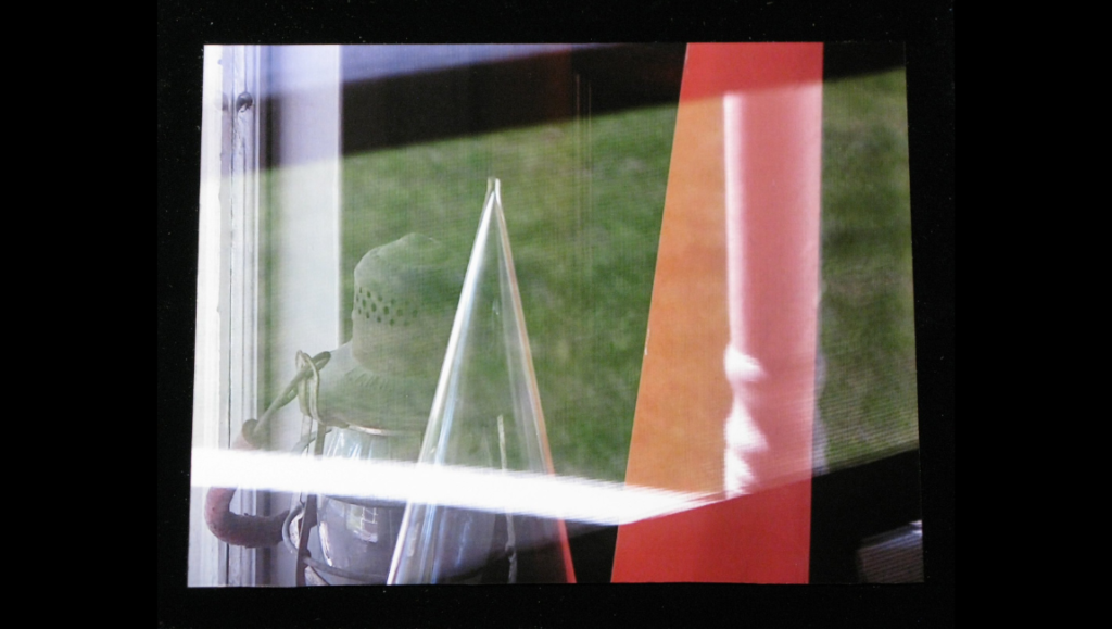 Barry Gerson film still. Glass pyramid, vintage lantern, and red post seen through a window. Anthology Film Archives.