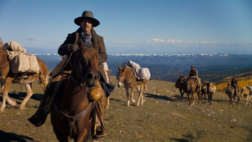 Kevin Costner in Horizon: An American Saga riding a horse. Western film scene with horses and mountainous landscape.