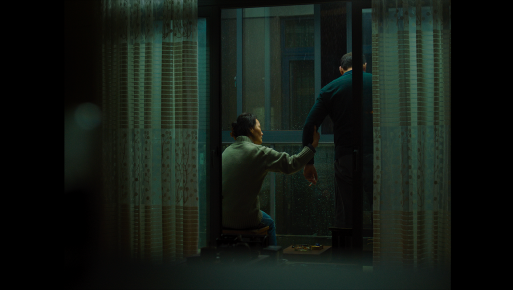 Some Rain Must Fall film scene. Woman holds man's hand near window. Tribeca '24 review. Qiu Yang movie still.