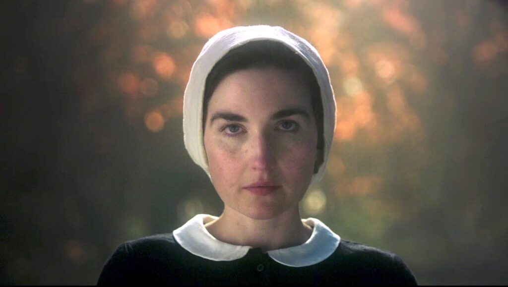 Some Rain Must Fall film still: Woman in traditional witch attire, white bonnet and collar, dark dress. Tribeca '24 review.