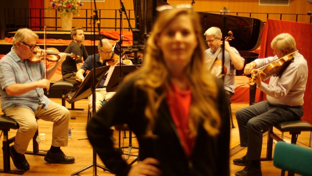 Constanze Ruhm's FIDMarseille '24 film review. Orchestra playing, woman in foreground. Avant Qu'il Ne Soit Trop Tard film scene.