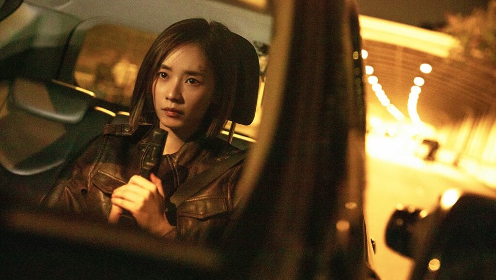 Customs Frontline movie still: Woman in car, holding gun. Action film scene.