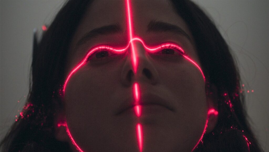 Electrophilia film still from Fantasia Fest 2024. Woman's face illuminated with red laser lines. Sci-fi movie scene.