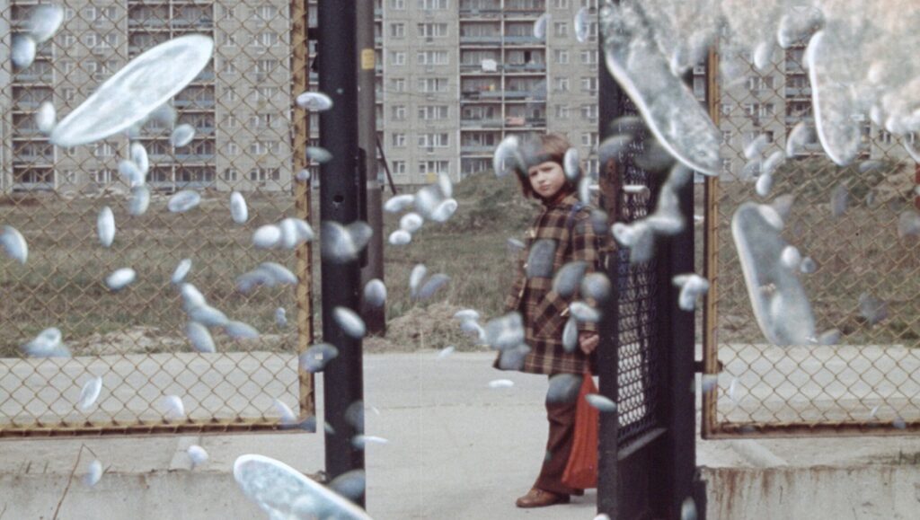 Still from Life Story film. Girl at gate with floating shapes. FIDMarseille review.