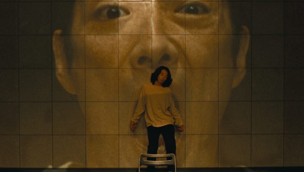 Kyrie Japan Cuts '24 review: A woman stands before a giant face projected on a tiled wall in Shunji Iwai's film.
