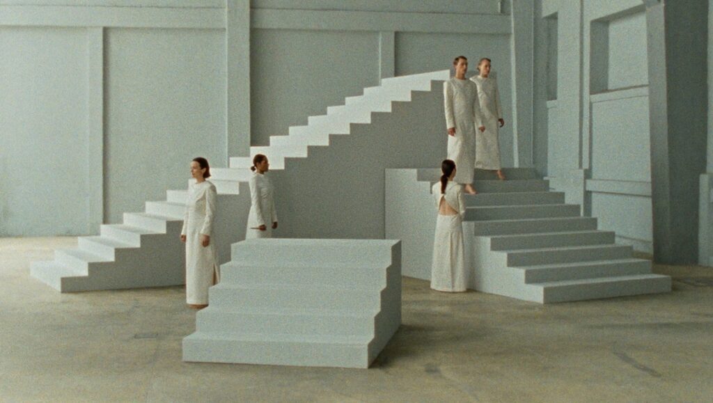 Land Without Words film still. Women in white dresses on stairs, FIDMarseille '24 review.