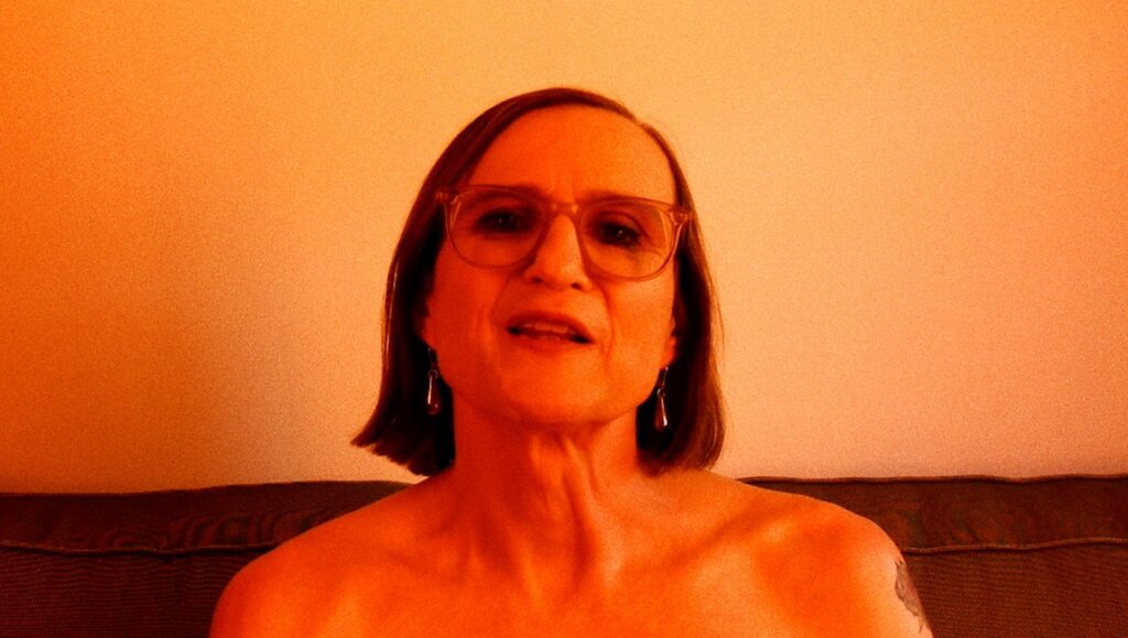 Still from Life Story (Jessica Dunn Rovinelli, FIDMarseille). Woman with glasses, orange lighting.