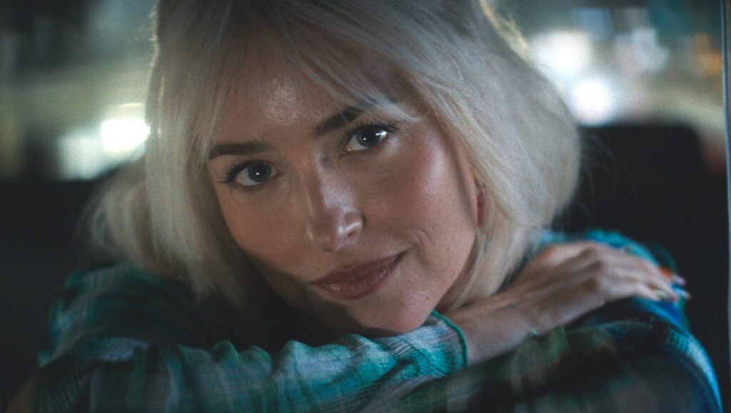 Dakota Johnson in Daddio (2024). Close-up of actress with blonde hair, wearing a patterned shirt. Movie review.