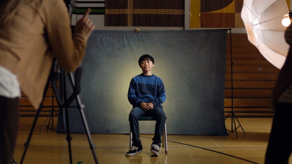 Dìdi film still: Sean Wang's character sits for a portrait. Camera and lighting equipment surround him.