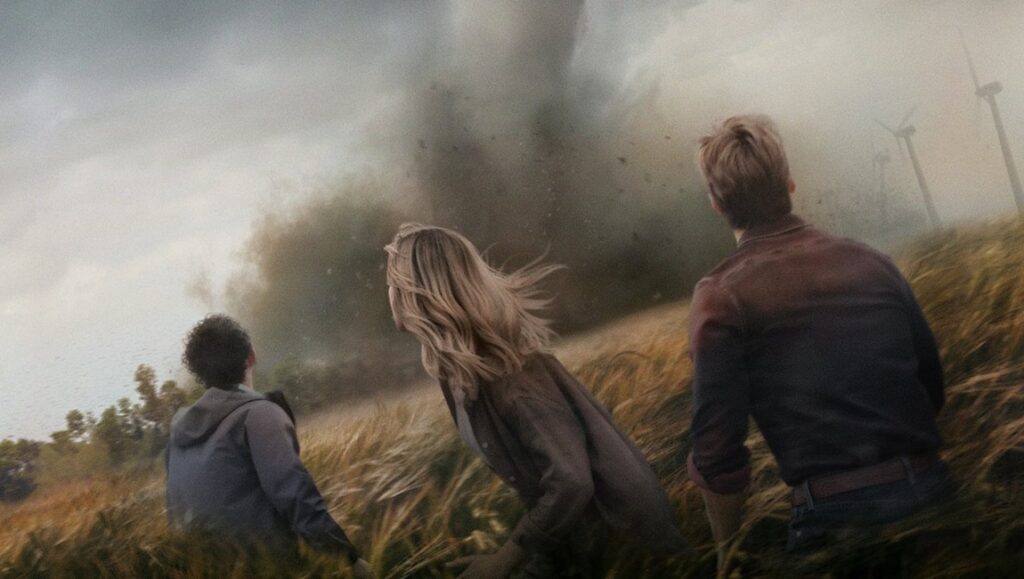Twisters movie scene: People looking at a tornado in a field with wind turbines.