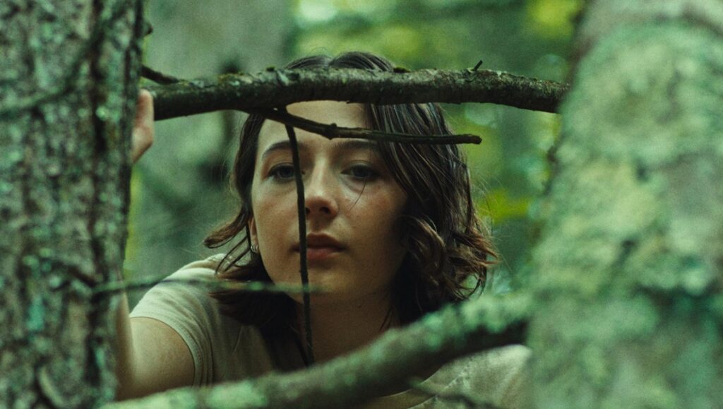 Good One movie still. Woman in forest, looking through branches. India Donaldson film review.