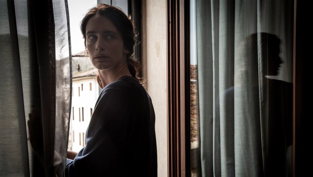 Locarno Film Festival 2024 — Dispatch 2: Drowning Dry, Transamazonia, Four Evil Deeds La vita accanto film still from Locarno Film Festival. Woman looks out window with shadow. Drama, cinema.