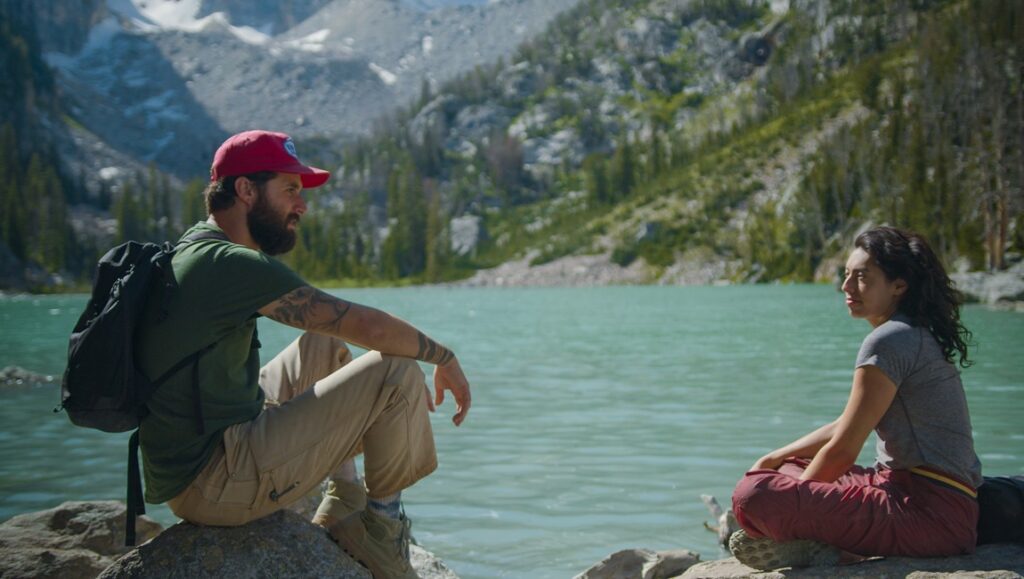 Peak Season movie review: Two hikers at a glacial lake with mountain backdrop. Outdoor adventure, travel.