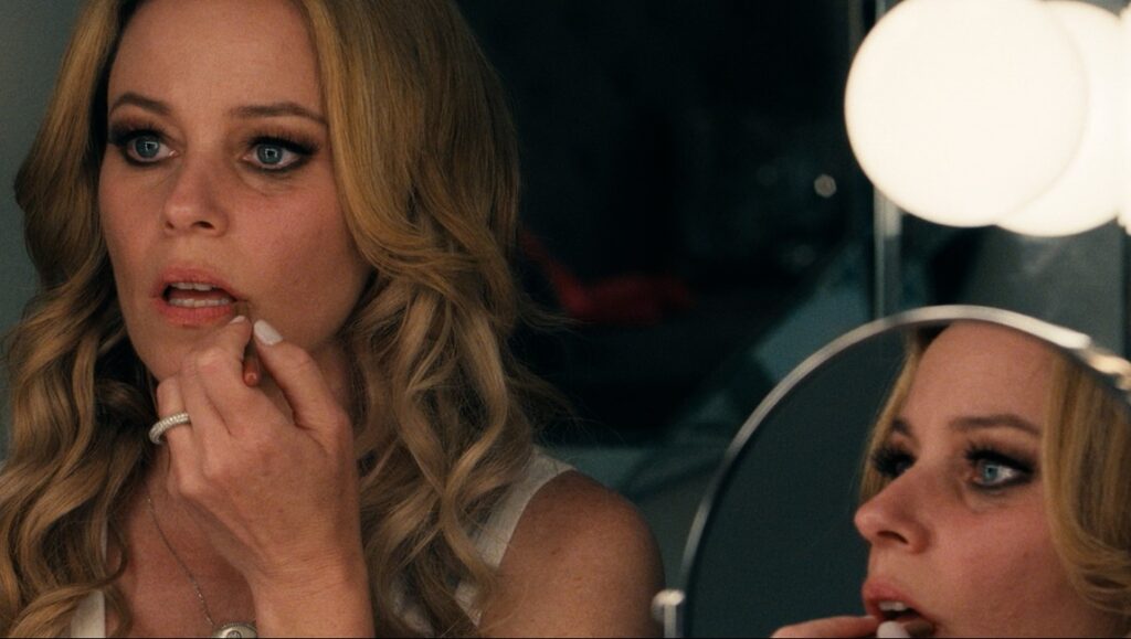 Woman applying skincare product. Blonde hair, fair skin, and visible makeup. Mirror reflection.