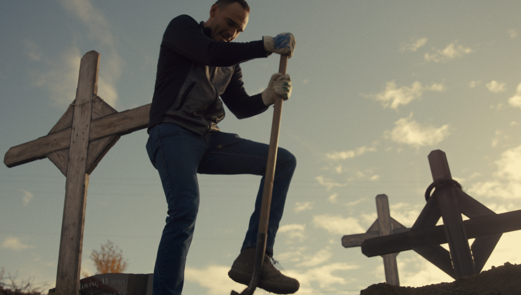Sugarcane review image: Man digging grave with crosses. Cemetery scene.