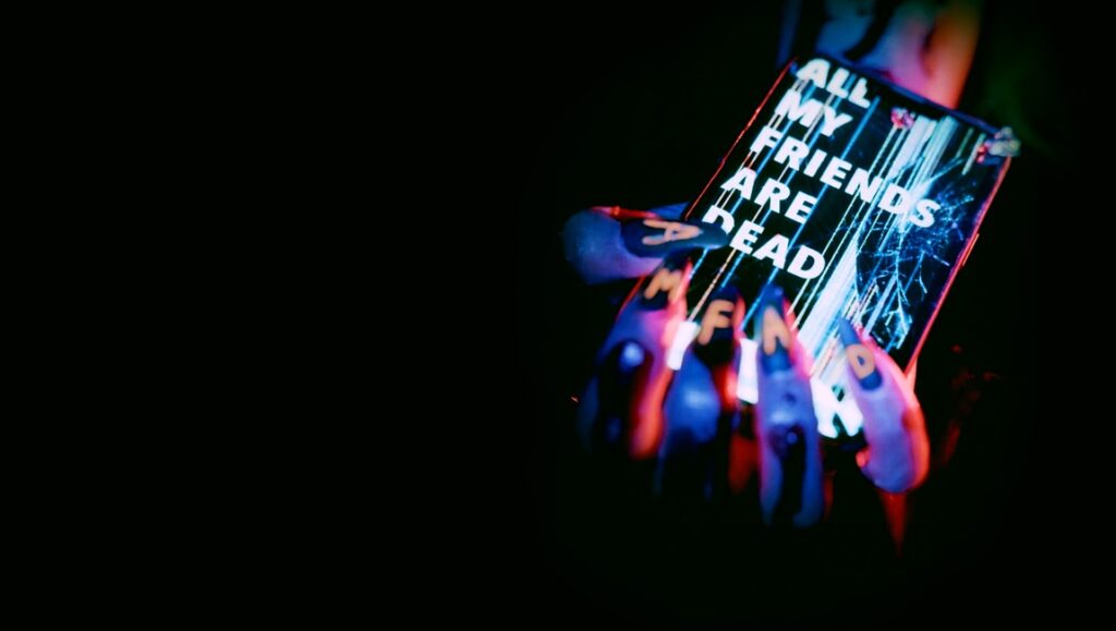 #AMFAD movie review image. Hand holding cracked phone with All My Friends Are Dead text.