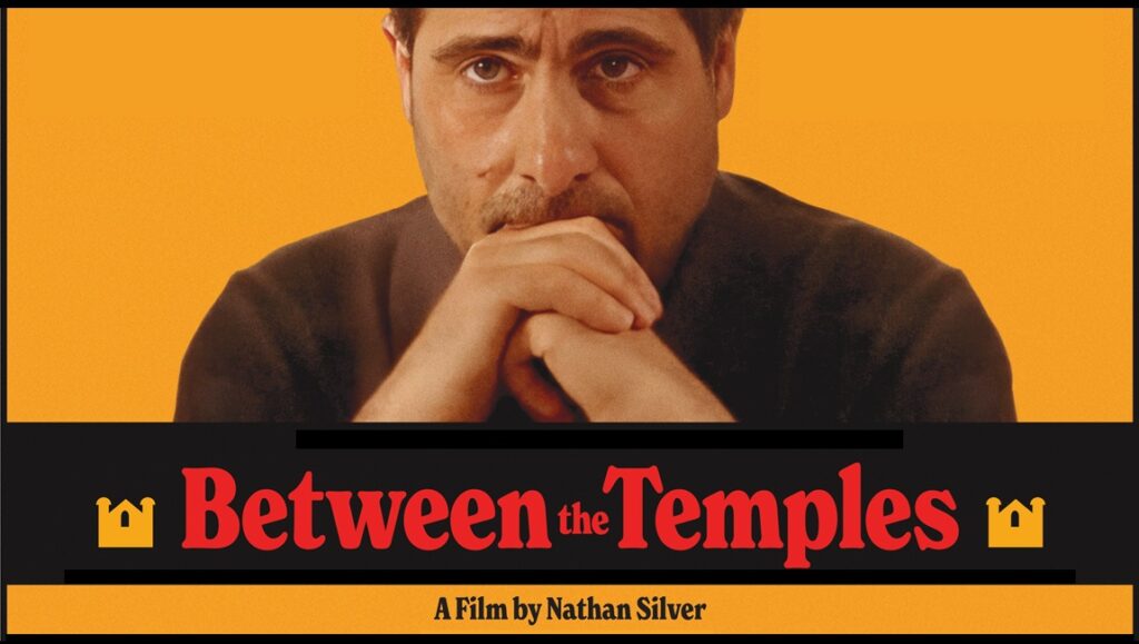 Between the Temples movie poster. A film by Nathan Silver. Man with hands clasped. Indie film.