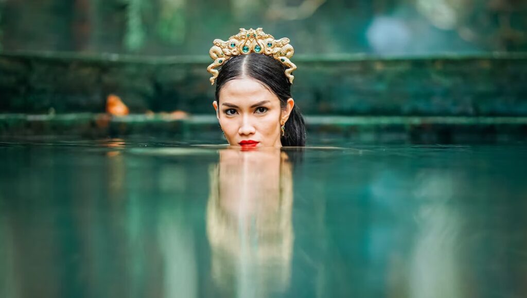 Dancing Village: The Curse Begins film still. Woman in water with ornate headpiece.