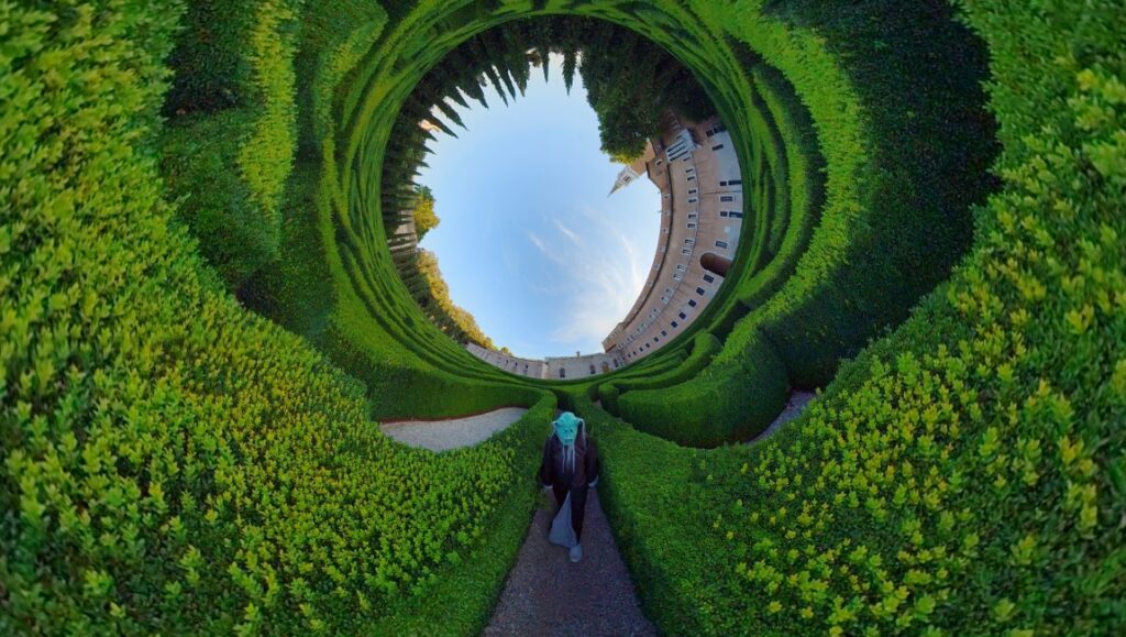 Person in a hedge maze at Locarno '24 film review. Green labyrinth with building and blue sky. Virgil Vernier film.