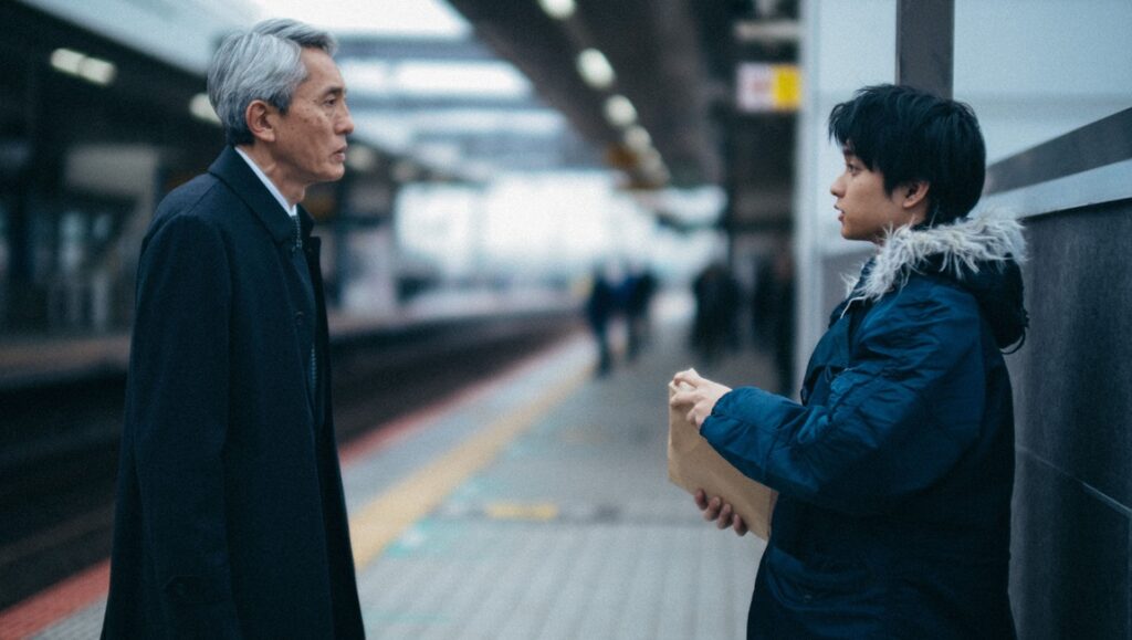 Still from Kiyoshi Kurosawa's Cloud film review. Two men face each other on a train platform.