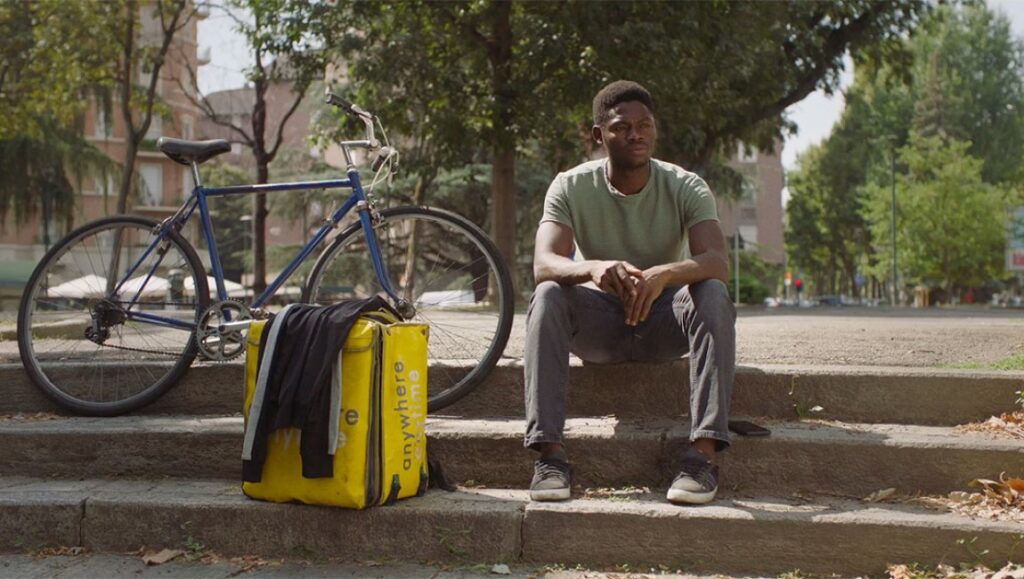 Delivery driver sitting on steps with bicycle and anywhere delivery bag. Food delivery job.