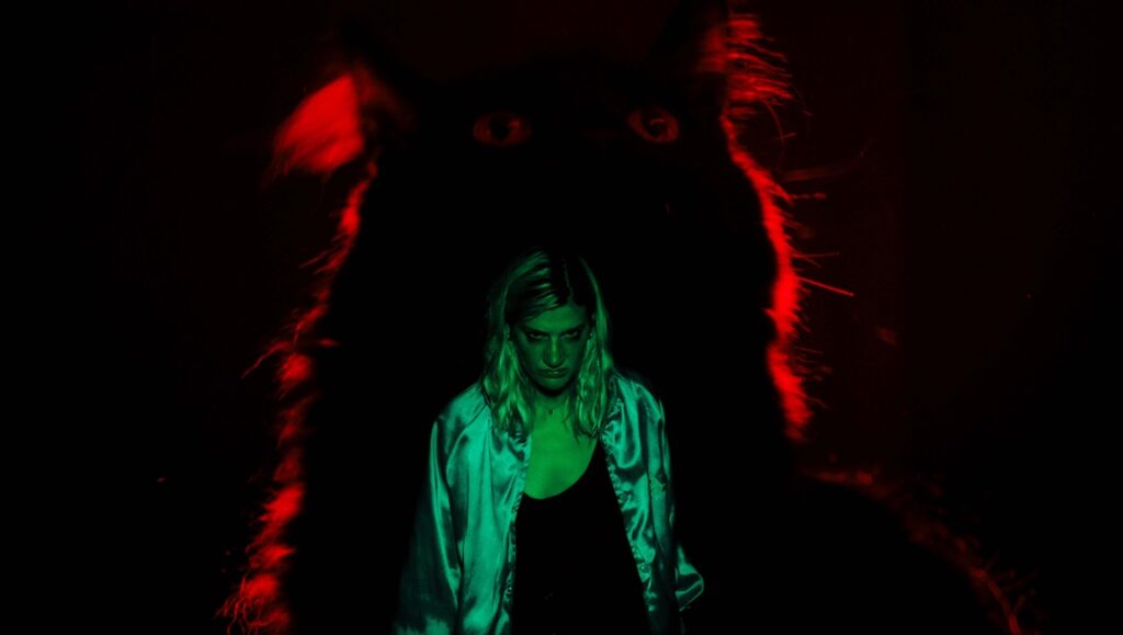 Mary Dauterman's Booger review image. Woman in green light with a large, shadowy monster behind her in red light.