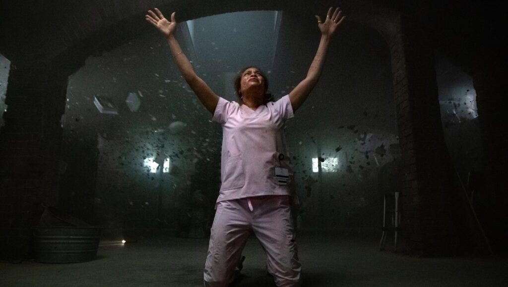 Still from Lee Daniels' The Deliverance movie. Woman kneeling with arms raised in dark room.