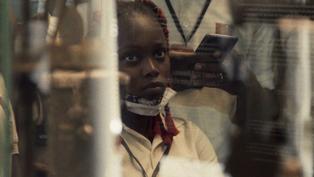 Seeds film still: A young Black girl, face mask askew, looks up. Red braids. TIFF '24 review.